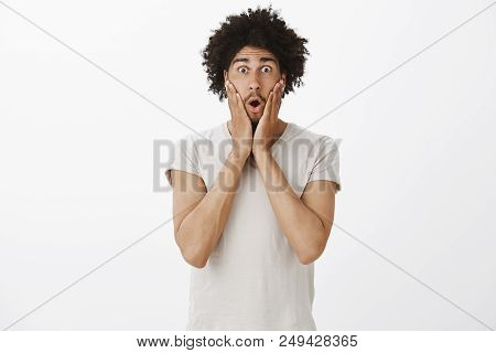 Studio Shot Of Attractive Hispanic Young Man With Curly Hair And Moustache, Gasping, Saying Wow Whil