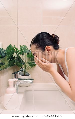 Woman Washing Her Face With Water Above Bathroom Sink.