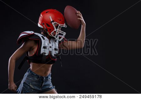 Sportive Serious Woman In Helmet Of Rugby Player Holding Ball In Stuio On Black Background. Copy Spa
