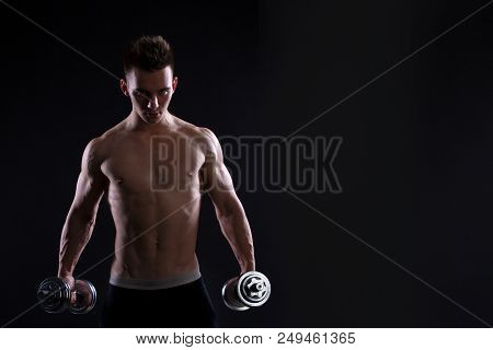Athletic Young Man With A Dumbbell On A Black Background. Naked Torso, Muscular Body. Strong Chest A