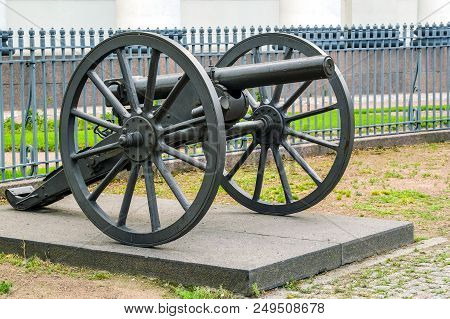 Vintage Cast Iron Cannon On A Carriage With Large Wheels. Against The Fence.