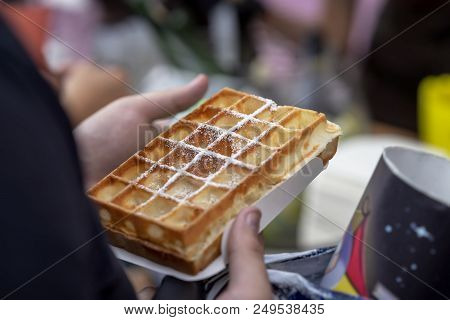 Belgian Fresh Warm Waffle With Powdered Sugar In The Hands Of The Buyer. Gastronomic Dainty Products