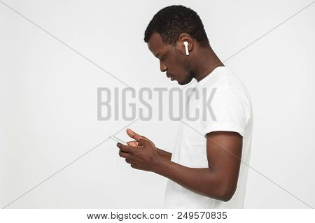 Side Shot Of Young African Man Isolated On Gray Background Holding Smartphone, Browsing Webpages Or 