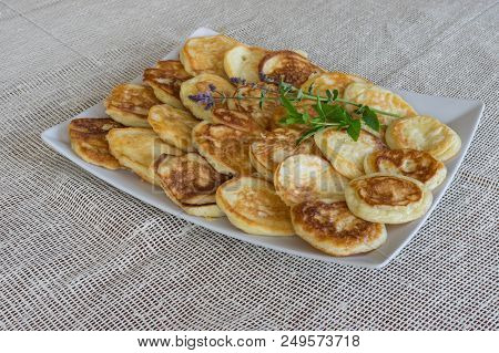 Plate Full Of Pancakes With Branches Of Mint Standing On A Table Covered With Textile Table-cloth