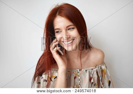Isolated Shot Of Modern Active Young Lady With Straigh Ginger Hair Smiling Broadly While Speaking On