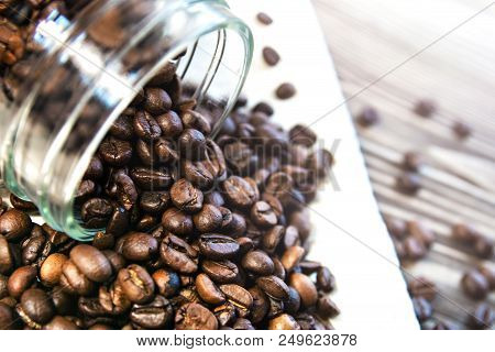 Coffee Beans Scattered From A Jar On A Towel On A Wooden Table.