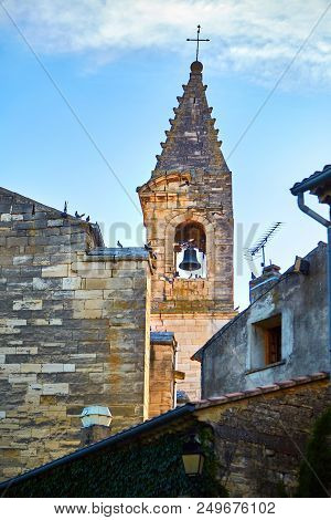 View Of The Church Tower With A Bell And A Cross And Roofs Of Houses With Sitting Pigeons