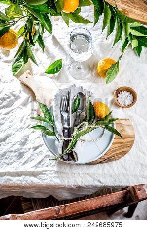 Table Setting With White Plate, Cutlery, Linen Napkin And Orange Tree Branch Decoration On White Lin