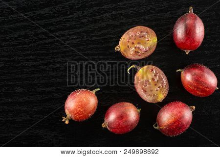Group Of Five Whole Two Halves Of Fresh Red Gooseberry Hinnomaki Variety Flatlay On Black Wood