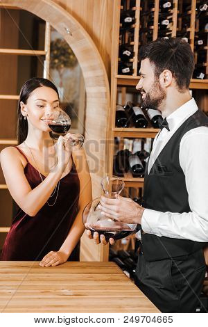 Wine Steward Holding Decanter Of Wine In Front Of Female Client At Wine Store