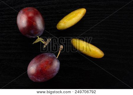 Group Of Two Whole Two Slices Of Fresh Violet-blue Plum Vibrant Moyer Variety Flatlay On Black Wood
