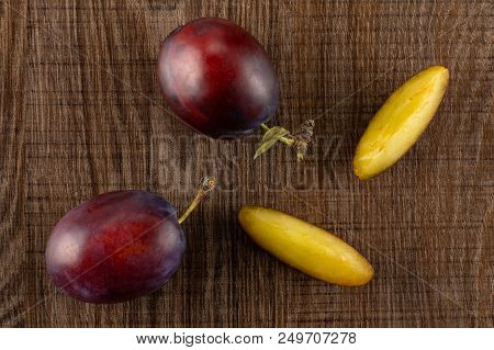 Group Of Two Whole Two Slices Of Fresh Violet-blue Plum Vibrant Moyer Variety Flatlay On Brown Wood