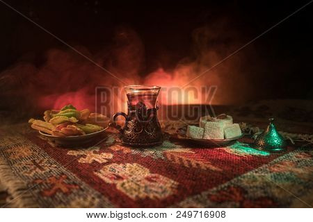 Arabian Tea In Glass With Eastern Snacks On A Carpet On Dark Background With Lights And Smoke. Easte