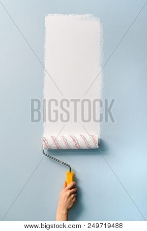 A Hand With A Roller Paints A Blue Wall With White Paint