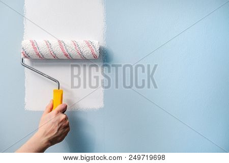 A Hand With A Roller Paints A Blue Wall With White Paint
