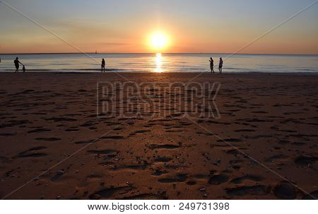 People Enjoy The Sunset At Mindil Beach. The Sun Casts Orange Shades Across An Evening Sky At Mindil