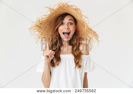 Portrait closeup of young pretty woman 20s wearing big straw hat showing index finger up like having idea isolated over white background