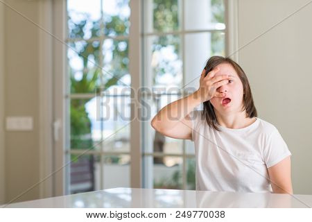 Down syndrome woman at home peeking in shock covering face and eyes with hand, looking through fingers with embarrassed expression.