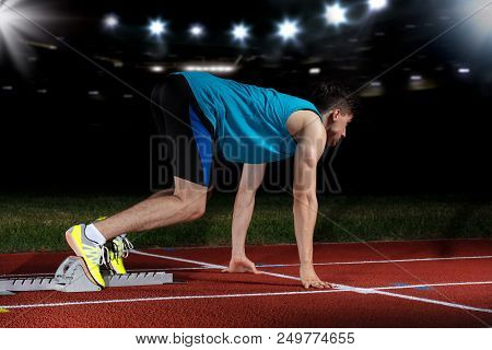 Sprinter Leaving Starting Blocks On The Running Track In Front Of Big Modern Stadium With Lights And