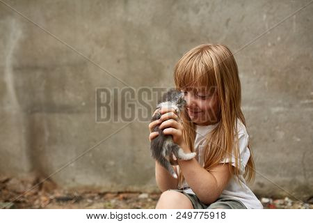 Portrait Of A Little Girl With Long Matted Hair And In Shabby Clothes Playing With Stray Kitten Sitt