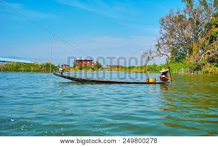 Burmese Villager Floats Along The Inle Lake In His Canoe, Sitting On The Edge And Pusshing Off The B