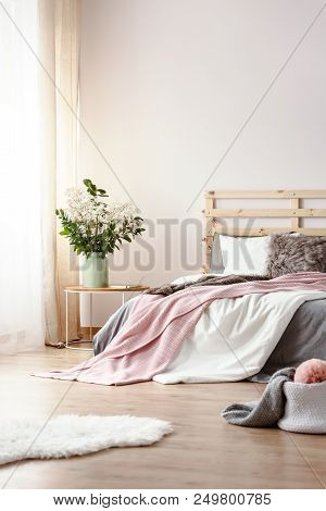 Fresh Plants In Ceramic Vase Standing On Bedside Table In White Bedroom Interior With Window With Cu