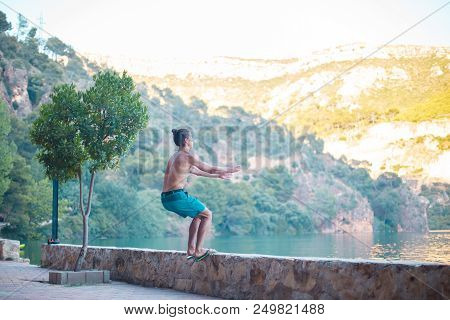 Young Man Doing A Side Flip Or Somersault While Practicing Parkour On A Lake In The Countryside.