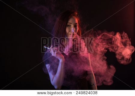 Portrait Of Asian Woman Smoking Vape Or E-cigarette In Neon Light At Black Background