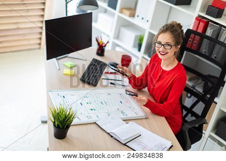 Beautiful Young Girl In Glasses And A Red Shirt Is Working In The Office. Photo With Depth Of Field.