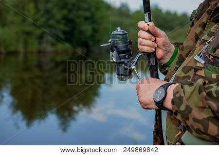 A Fisherman With A Fishing Rod. Close-up Of A Hand Holding A Spinning Rod And Twisting A Coil. Color