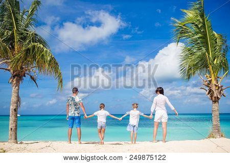 Back View Of Family Of Four In White On The Beach On Caribbean Vacation. Parents With Two Kids Betwe