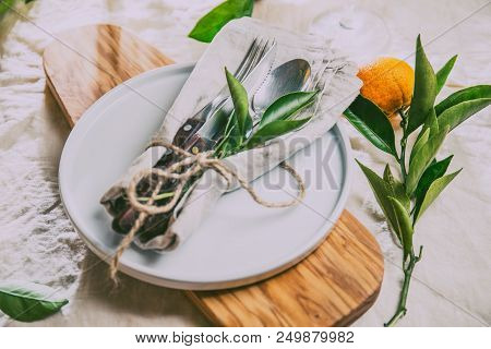 Table Setting With White Plate, Cutlery, Linen Napkin And Orange Tree Branch Decoration On White Lin