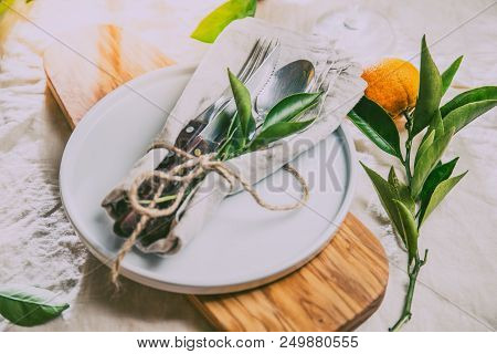 Table Setting With White Plate, Cutlery, Linen Napkin And Orange Tree Branch Decoration On White Lin