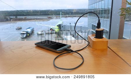 Charging A Mobile Phone Against A Background Of Refueling An Airplane