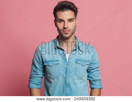 portrait of smiling handsome man wearing a denim shirt with rolled sleeves and standing near a white red wall