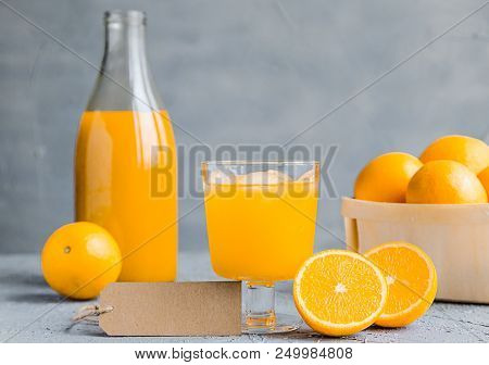 Orange Freshly-squeezed Juice In A Glass And Bottles On Grey Table.