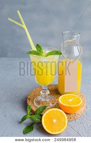 Orange Freshly-squeezed Juice In A Glass And Bottles On Grey Table.