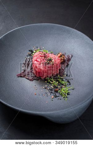Gourmet fish tartar raw from tuna fillet with seaweed, umeboshi and Japanese spice as closeup on modern design plate 