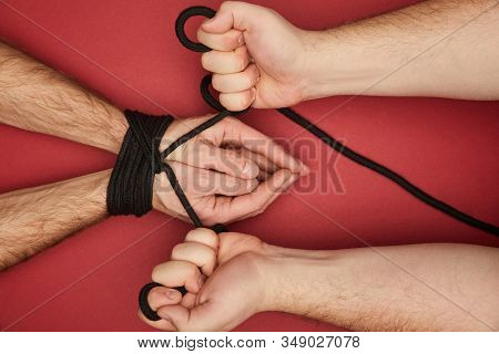 Cropped View Of Man Holding Rope On Tied Boyfriend Hands Isolated On Red