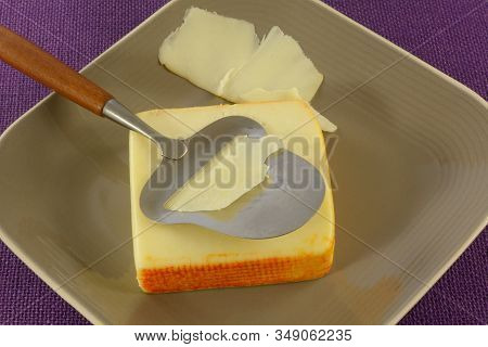 Block Of Muenster Cheese On Plate With Cheese Slicer Slicing Thin Slices Of Cheese