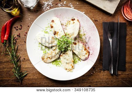 Cooked green mussels with parmegano and cream cheese served on white plate in restaurant