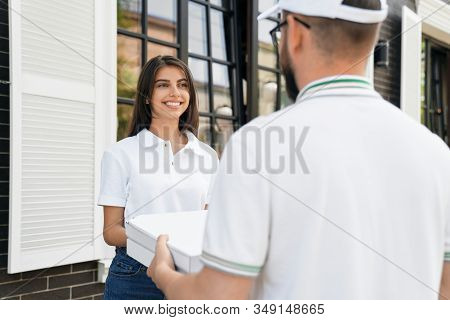 Close Up Of Young Deliveryboy In White Cap And Glasses Giving Two Boxes Of Pizza To Woman. Pretty Sm