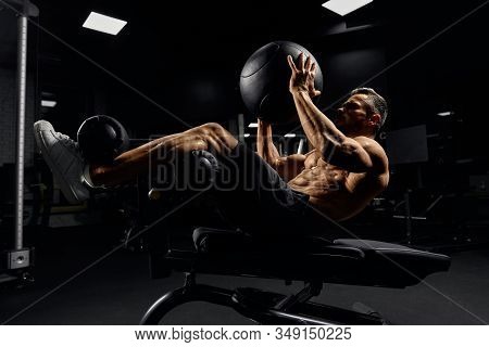 Side View Of Muscular Caucasian Man Training Abs With Ball, Lying On Special Bench In Gym. Handsome 