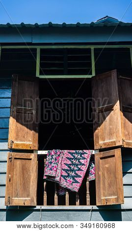 Batik Fabric Hanging On The Window Of Rumah Kampung Under The Bright Sunlight.