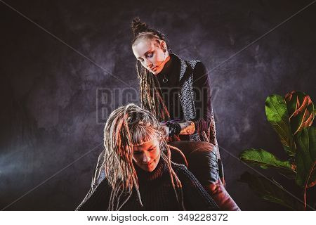 Woman With Long Dreadlocks Is Making Dreads For Blond Girl At Dark Room.