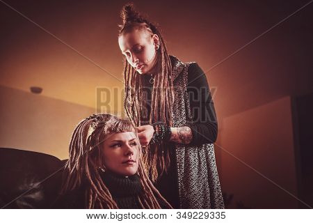 Attractive Dreadlock Master Is Working On Dreads For Pretty Blond Girl In The Dark Room.