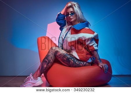 Avantgarde Portrait Of Young Woman With Tattoo On Her Leg, She Is Sitting On Bean Bag.