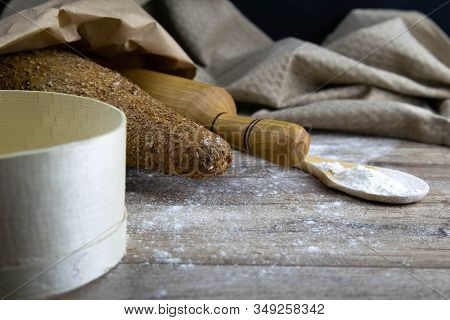 A Loaf Of Bread Along With Rocking For The Dough In A Craft Bag Stand On A Wooden Table, Next To It 