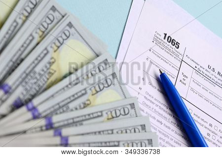 1065 Tax Form Lies Near Hundred Dollar Bills And Blue Pen On A Light Blue Background. Us Return For 