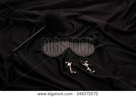 Feather Tickler, Mask And Nipple Clamps On Black Textile Background